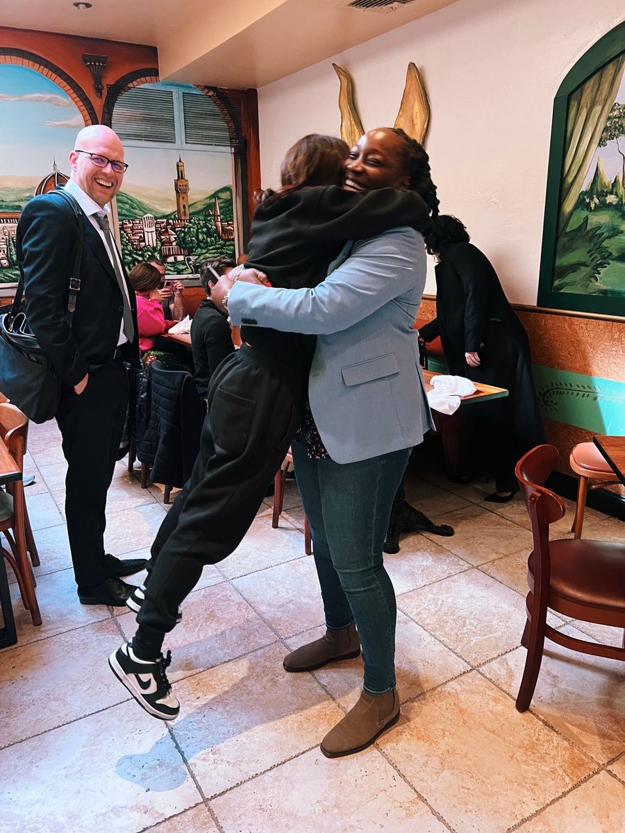 Kevin Williams smiling as two friends embrace at a celebration in a restaurant